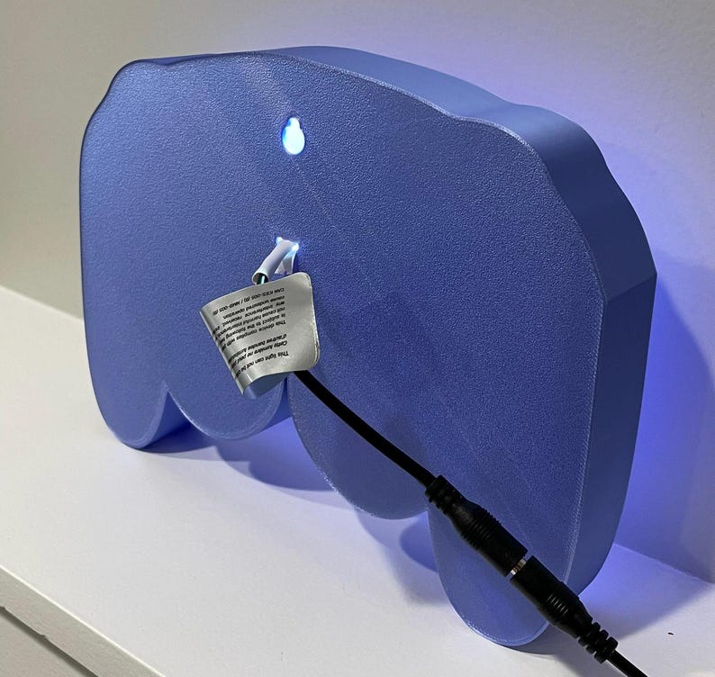 May include: A light blue, 3D printed, controller-shaped night light with a black cord and plug. The light is turned on and emits a blue glow.