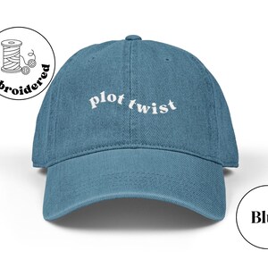 Puede incluir: Gorra de béisbol azul con las palabras "plot twist" bordadas en blanco en la parte delantera. La gorra tiene una visera curva y un diseño de seis paneles. Un pequeño logotipo bordado está en el lateral.
