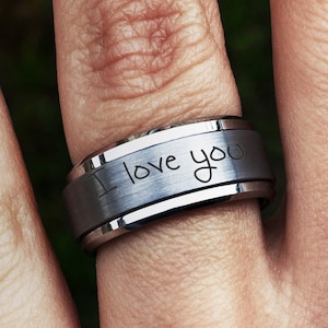 May include: A silver-toned metal band ring featuring a brushed matte center finish and polished beveled edges. The outer surface of the ring is engraved with the handwritten-style text "I love you" in a dark, clear font across the center band.