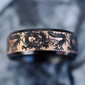 K&ouml;nnte beinhalten: Ein schwarzer Ring mit einer ros&eacute;goldenen Banderole, die mit einem Drachenmotiv verziert ist.
