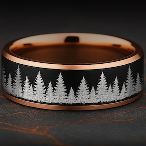 May include: A ring featuring a matte black outer band with a laser-engraved forest of pine trees in silver. The interior and the beveled edges of the band are finished in a polished rose gold tone, creating a contrast between the dark and metallic surfaces.