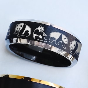 May include: A black and silver ring with a design of five pandas walking in a line. The ring is made of stainless steel and has a polished finish.