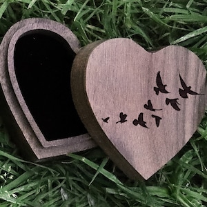 May include: A dark brown wooden heart-shaped box with a hinged lid. The box is open and the inside is black. The lid has a design of birds flying in a flock.