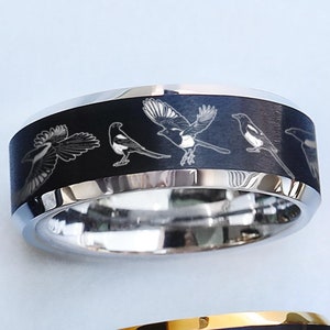 May include: A black and silver ring featuring an engraved design of four magpies. The ring is crafted from stainless steel and has a polished finish.