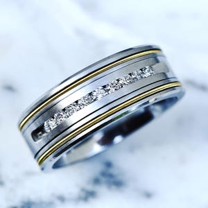 Puede incluir: Una alianza de plata y oro con una fila de pequeños diamantes engastados en el centro.