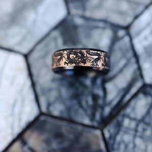 K&ouml;nnte beinhalten: Ein schwarzer und ros&eacute;goldener Ring mit einem Drachenmotiv. Der Ring liegt auf einer grauen und wei&szlig;en gekachelten Oberfl&auml;che.