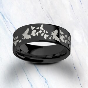 Pu&ograve; includere: Un anello in carburo di tungsteno nero con un design a farfalla argentato. L'anello &egrave; inciso con pi&ugrave; farfalle.
