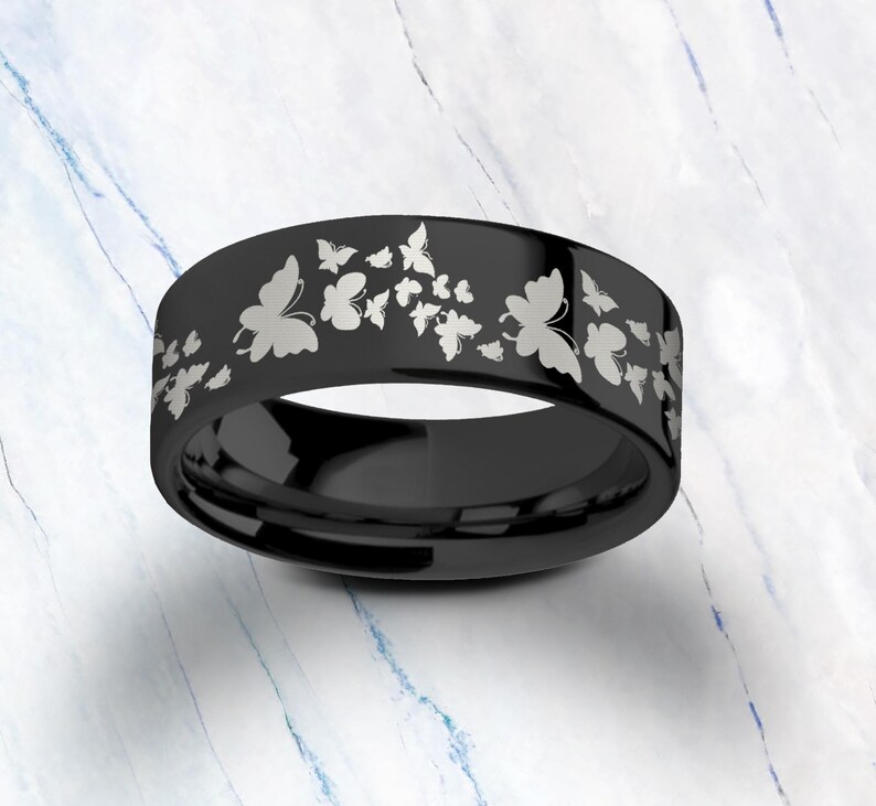Pu&ograve; includere: Un anello in carburo di tungsteno nero con un design a farfalla argentato. L'anello &egrave; inciso con pi&ugrave; farfalle.