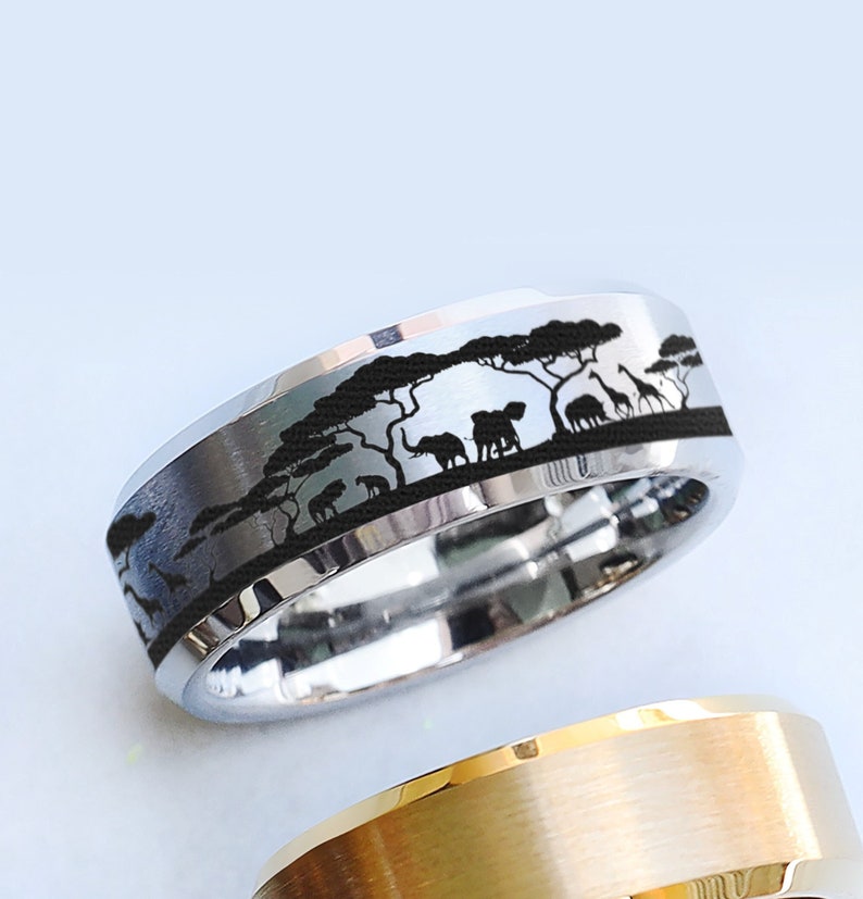 May include: A silver ring with a black inlay featuring a silhouette of an African savanna scene with trees, elephants, giraffes, and other animals.