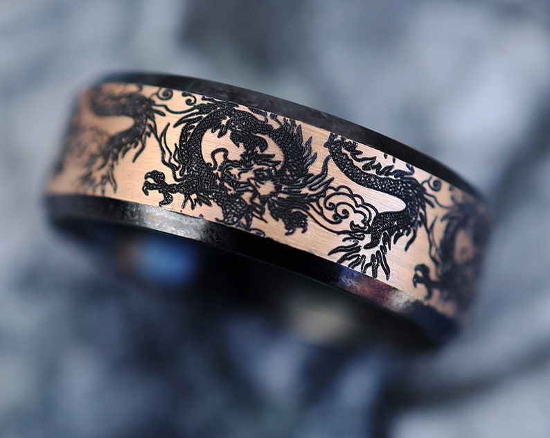 K&ouml;nnte beinhalten: Ein schwarzer und ros&eacute;goldener Ring mit einem gravierten Drachenmuster auf der Band.