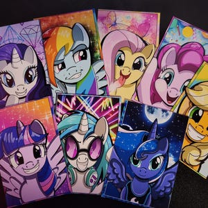May include: A collection of colorful, rectangular art prints featuring various cartoon ponies. Each print showcases a different pony character with unique designs and backgrounds, including diamonds, rainbows, and a night sky.