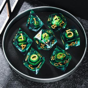 May include: A set of seven polyhedral dice in a black tray. The dice are transparent green with gold numbering and a green eye design inside. The dice include a d4, d6, d8, d10, d12, d20, and a percentile die.