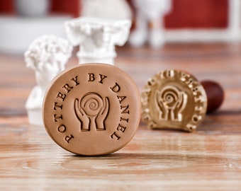 May include: A brown clay stamp with the text "POTTERY BY DANIEL" and a design of two hands holding a spiral.