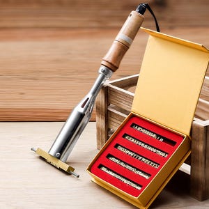 May include: A metal branding iron with a wooden handle and a heating element, accompanied by a yellow box containing five rows of interchangeable brass letter stamps set against a red velvet-like interior lining for custom marking.