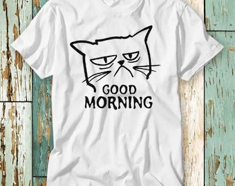 Könnte beinhalten: Weißes T-Shirt mit einer schwarz-weißen Illustration einer Katze mit dem Text "GOOD MORNING" darunter.