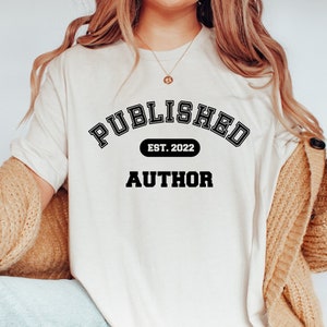 May include: White t-shirt with black text that reads "PUBLISHED EST. 2022 AUTHOR" in a collegiate-style font.