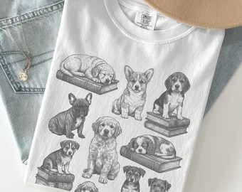 May include: White t-shirt featuring a collection of sketched puppies on books. The shirt is paired with light blue jeans, a gold necklace, and a beige hat. The word "WHITE" is printed at the bottom of the image.