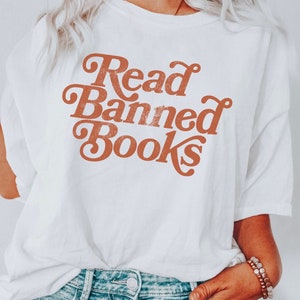 May include: White t-shirt with the text "Read Banned Books" in a retro orange font.