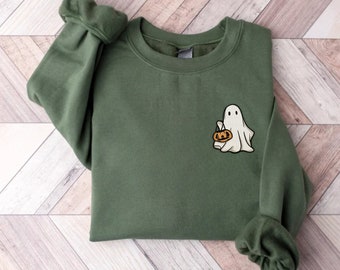 May include: An olive green sweatshirt with a small embroidered ghost holding a pumpkin. The ghost is white with black eyes and a smiling mouth. The pumpkin is orange with a black face. The sweatshirt has a crew neck and long sleeves.