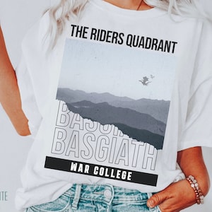 K&ouml;nnte beinhalten: Wei&szlig;es T-Shirt mit einem Grafikdesign, das eine Bergkette, einen Drachen, der am Himmel fliegt, und den Text "The Riders Quadrant", "Basgiath" und "War College" zeigt.