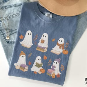 Blue Jean Comfort Colors shirt featuring six cozy reading ghosts with books, pumpkins, autumn leaves, scarves, hats, and seasonal book lover details.