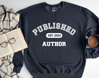 以下が含まれることがあります： ダークヘザーグレーのトレーナーに、白い文字で「Published Est. 2023 Author」と書いてあります。