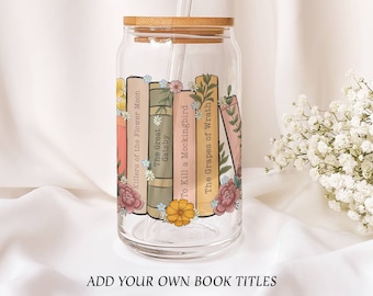 May include: A clear glass tumbler with a bamboo lid and a straw. The tumbler is decorated with a design of books and flowers. The book titles include "Killers of the Flower Moon", "The Great Gatsby", "To Kill a Mockingbird", and "The Grapes of Wrath".