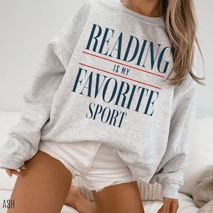 May include: A grey sweatshirt with the text "Reading is my favourite sport" printed on it in navy blue and red.