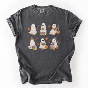 Pepper Comfort Colors shirt featuring six bookish ghosts reading books with pumpkins, fall leaves, cozy hats, scarves, and warm drinks.