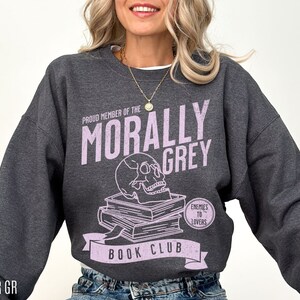 Puede incluir: Una sudadera gris jaspeada con un gr&aacute;fico de calavera y huesos cruzados y el texto "Proud Member of the Morally Grey Book Club. Enemies to Lovers".