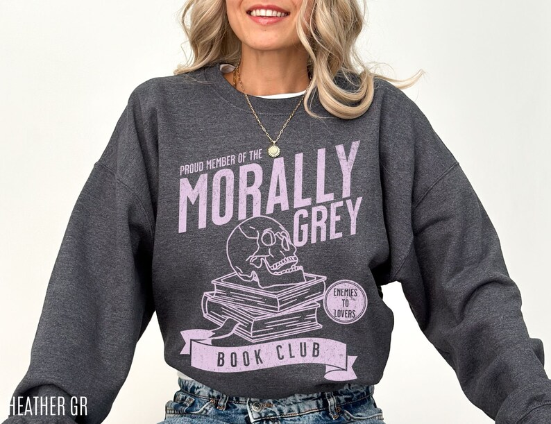 Puede incluir: Una sudadera gris jaspeada con un gr&aacute;fico de calavera y huesos cruzados y el texto "Proud Member of the Morally Grey Book Club. Enemies to Lovers".