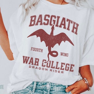 May include: White t-shirt with a red graphic design featuring a dragon and the text "Basgiath Fourth Wing War College Dragon Rider".