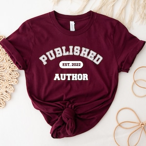 May include: Burgundy t-shirt with white text that reads "Published Est. 2022 Author".