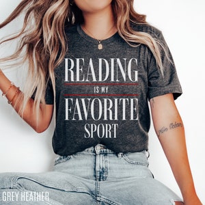 Może przedstawiać: Szary t-shirt z melanżu z nadrukiem "Reading is my favorite sport" w kolorze białym. Tekst jest oddzielony dwiema czerwonymi liniami.