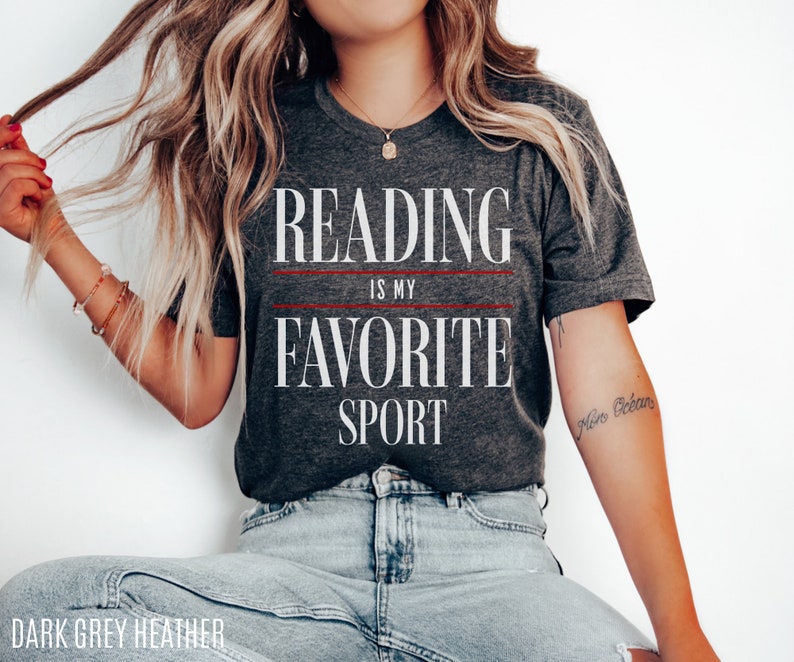 Może przedstawiać: Szary t-shirt z melanżu z nadrukiem "Reading is my favorite sport" w kolorze białym. Tekst jest oddzielony dwiema czerwonymi liniami.