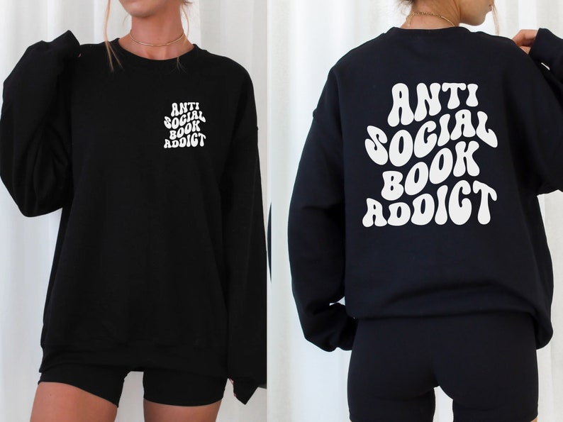 May include: Black sweatshirt with the text "ANTI SOCIAL BOOK ADDICT" in white, on the front left chest and back. The sweatshirt is a long-sleeved crew neck style. The text has a retro, wavy font.