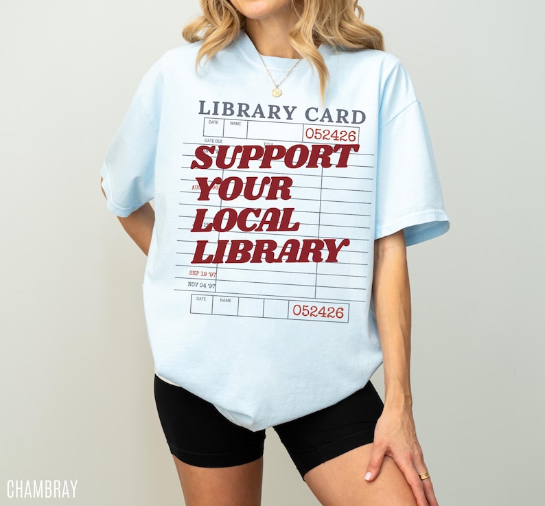 Woman wearing oversized chambray blue t shirt with retro library card design and support your local library bold red text