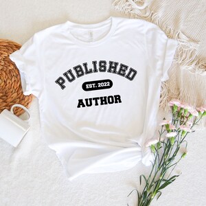 May include: White t-shirt with black text that reads "PUBLISHED EST. 2022 AUTHOR" in a collegiate font.