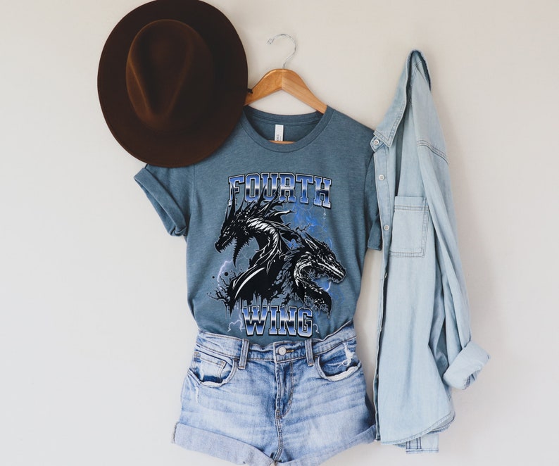 K&ouml;nnte beinhalten: Ein blaues T-Shirt mit einem schwarzen Drachen-Motiv und dem Text "FOURTH WING" in blauen und wei&szlig;en Buchstaben.