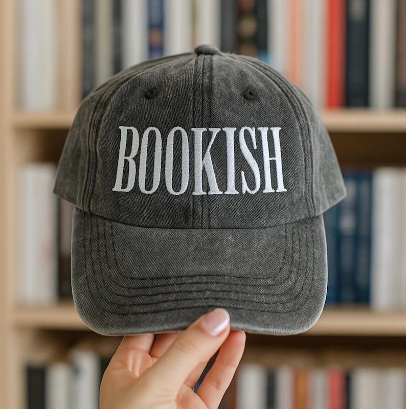 May include: A gray baseball cap with the word "BOOKISH" embroidered in white. The hat has a curved brim and a classic, casual style, perfect for book lovers.
