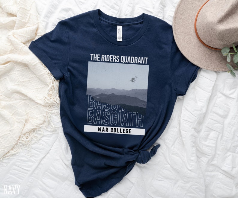 K&ouml;nnte beinhalten: Ein marineblaues T-Shirt mit einem grafischen Design, das eine Bergkette und den Text "The Riders Quadrant, Basquiat, War College" zeigt.