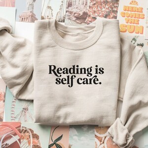 May include: A beige sweatshirt with the text "Reading is self care." printed in black.