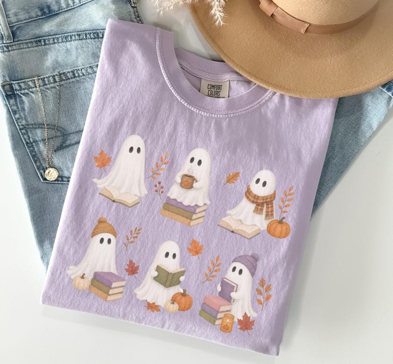 Orchid Comfort Colors shirt featuring a whimsical book lover ghost design with six reading ghosts, stacked books, pumpkins, fall foliage, knit hats, and a warm drink.