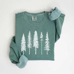 May include: A teal green sweatshirt with a white print of five trees. The sweatshirt is folded in half and the sleeves are rolled up.