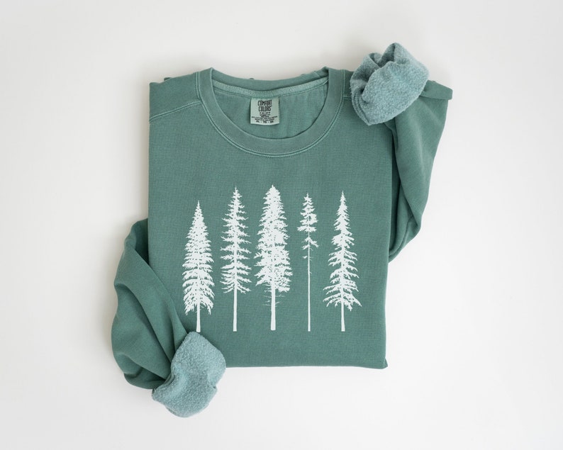 May include: A teal green sweatshirt with a white print of five trees. The sweatshirt is folded in half and the sleeves are rolled up.