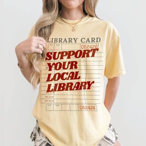 Woman wearing oversized yellow butter t shirt with retro library card design and bold support your local library lettering