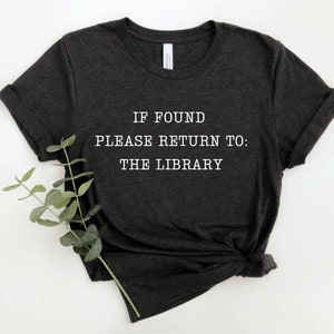 May include: A dark gray t-shirt with white text that reads "IF FOUND PLEASE RETURN TO: THE LIBRARY".