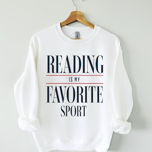 May include: White sweatshirt with the text "READING IS MY FAVORITE SPORT" in navy blue and red.