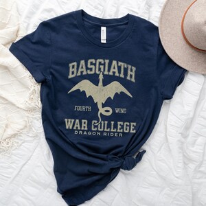 May include: Navy blue t-shirt with a white graphic of a dragon and the text "Basgiath Fourth Wing War College Dragon Rider".