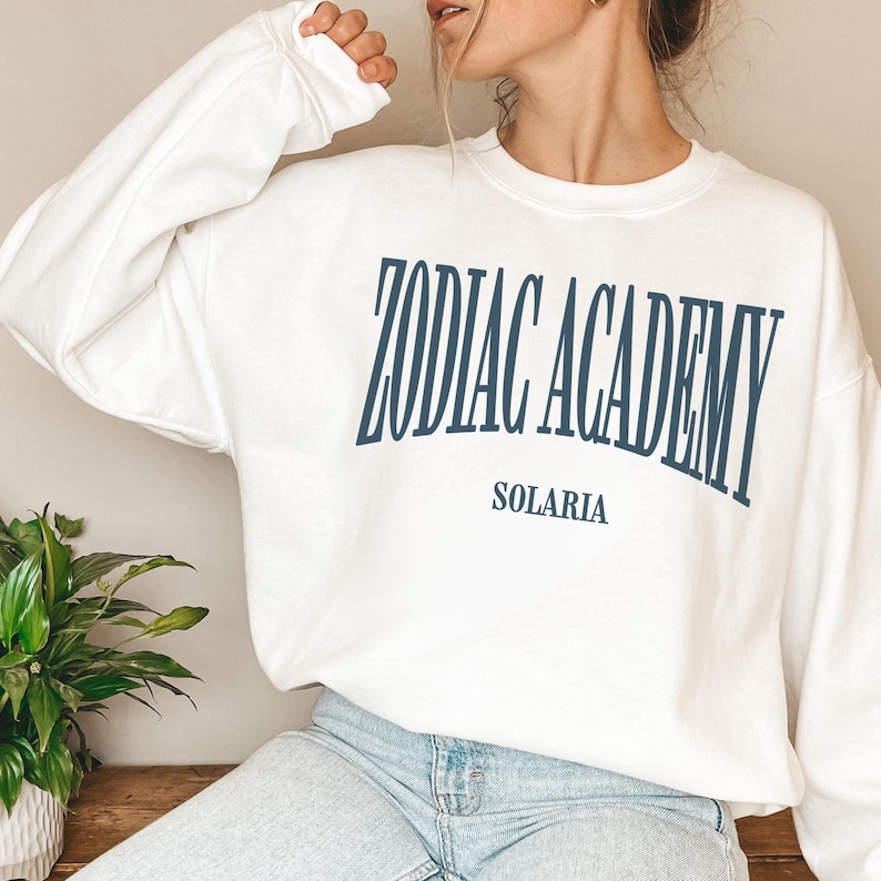 May include: White sweatshirt with the text "Zodiac Academy" in blue lettering and "Solaris" in smaller blue lettering below.